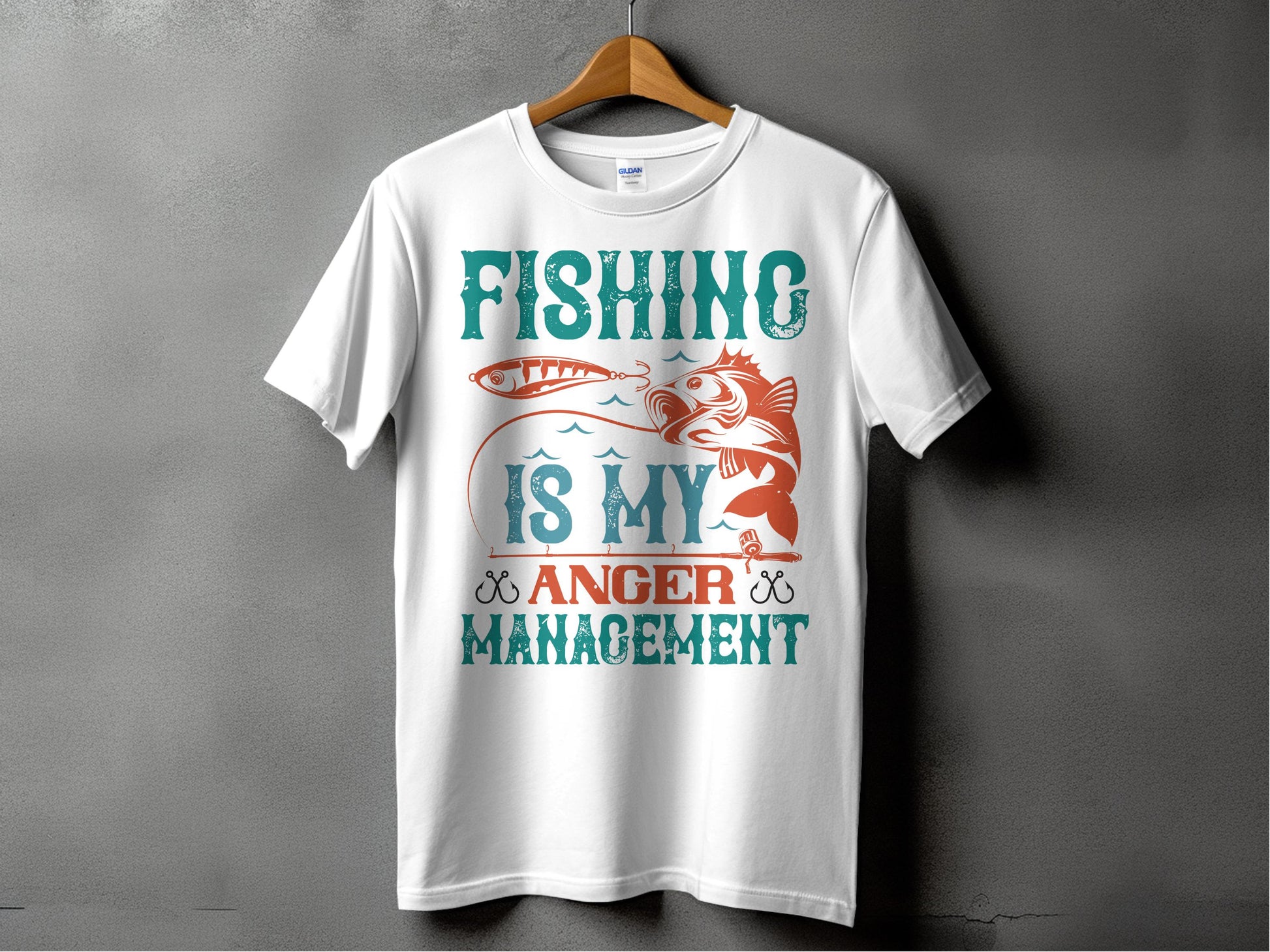 A white fishing T-shirt from Garment Graphics hangs on a wooden hanger against a gray background, featuring the bold design Fishing Is My Anger Management with teal and orange fish and lure images, ideal for any fishing enthusiast.