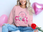 A person with long wavy hair, cross-legged and holding a red rose, sports a Garment Graphics pink sweatshirt with Just be cool, Rock and Roll. Ideal for fashion lovers, pink heart-shaped balloons in the background enhance the vibe for rock and roll headphone enthusiasts.