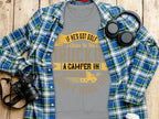 A flat lay of casual wear showcases a plaid shirt, headphones, and a camera surrounding a gray humorous sweatshirt by Garment Graphics. The shirt humorously reads, If hes got golf clubs in his truck or a camper in his driveway, dont hire him, using various fonts and colors.