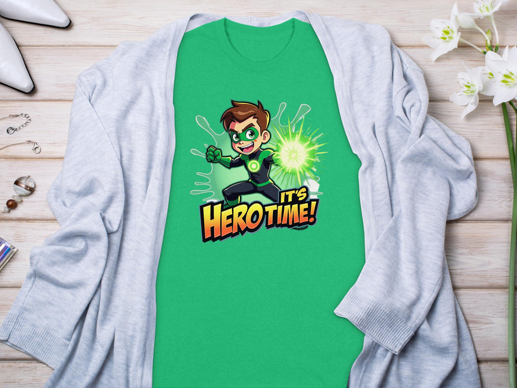 A vibrant green t-shirt from Garment Graphics showcases a superhero cartoon character holding a glowing green energy ball with the bold text Its Hero Time! Its paired with a light gray cardigan amidst jewelry and flowers on a wooden surface.