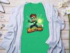 A vibrant green t-shirt from Garment Graphics showcases a superhero cartoon character holding a glowing green energy ball with the bold text Its Hero Time! Its paired with a light gray cardigan amidst jewelry and flowers on a wooden surface.