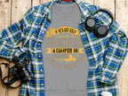 Garment Graphics gray t-shirt features a funny graphic with yellow and white text: If hes got golf clubs in his truck or a camper in his driveway, I dont hire him. The shirt is displayed on a wooden surface alongside a plaid shirt, headphones, and a camera.