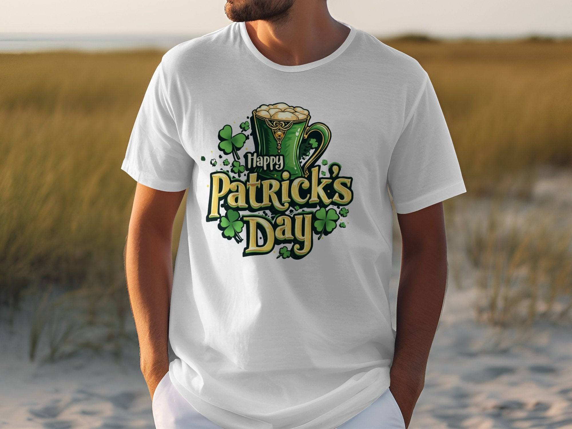 Dressed in a Garment Graphics Happy Patricks Day T-Shirt, featuring a beer mug and shamrocks, a person stands outdoors where sand meets grass, capturing the festive spirit of the occasion.