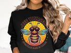 A woman with long, wavy hair sports a Garment Graphics Summer Edition Sweatshirt. It showcases a cartoon bee with sunglasses and a beard against a sunburst backdrop, alongside the phrase BEE YOURSELF, EVERYONE ELSE IS TAKEN. Unisex sizing ensures this vibrant style suits anyone.