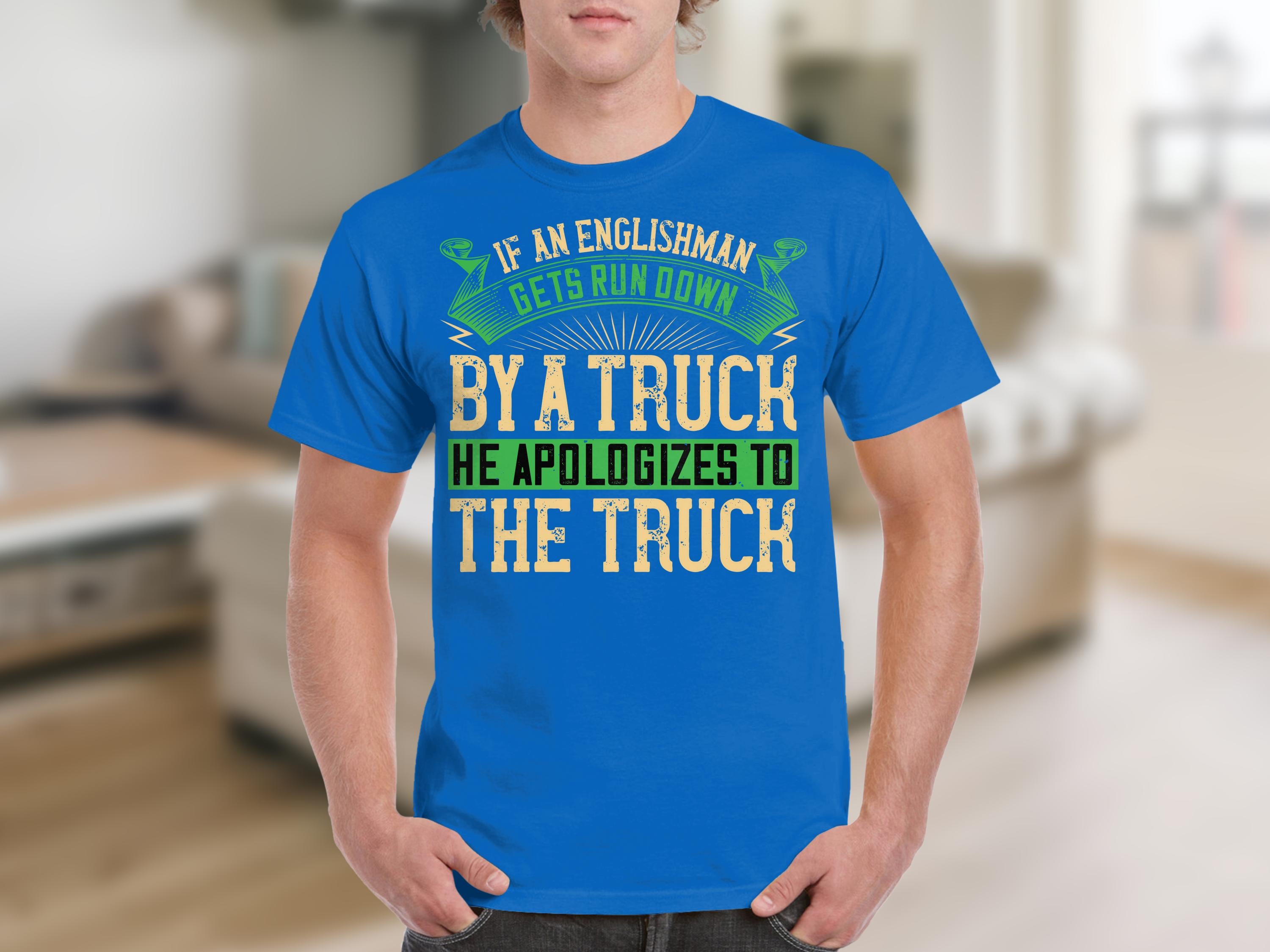 Sporting a blue T-shirt from Garment Graphics, the design humorously reads: If an Englishman gets run down by a truck, he apologizes to the truck, set against a blurry indoor living space, adding charm to this witty tribute to English politeness.