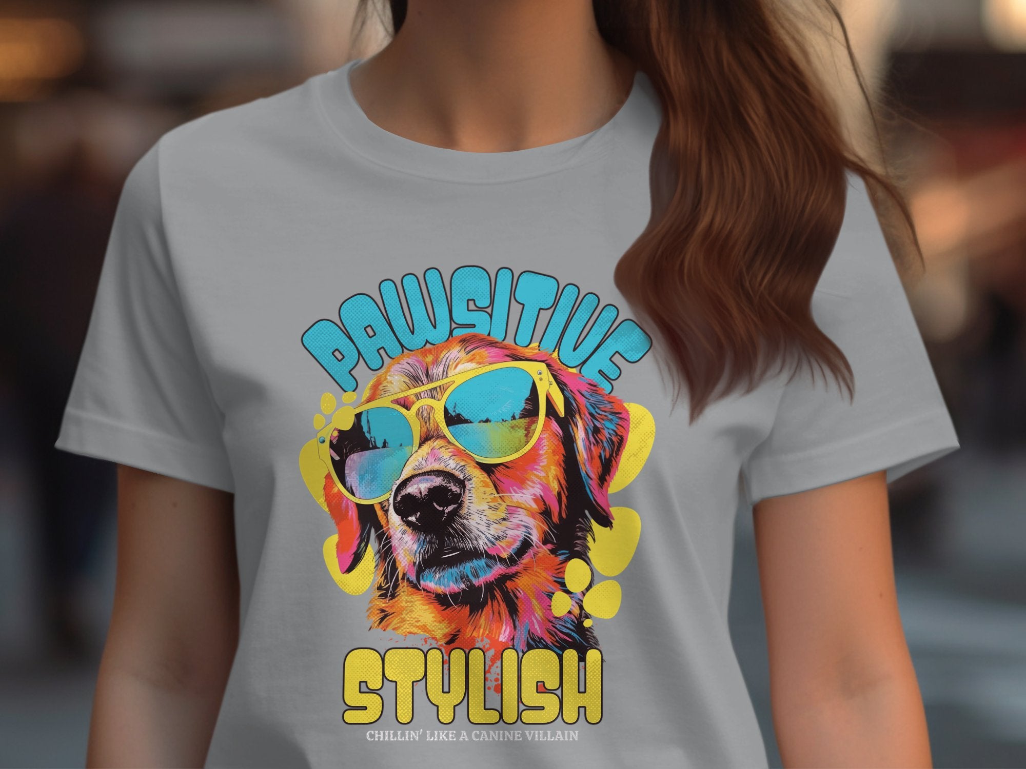 A woman wears a Garment Graphics gray Dog T-Shirt with a vibrant dog in sunglasses graphic. Pawsitive is bold in blue above, Stylish below, and the phrase Chillin like a canine villain at the bottom, expertly tailored to Womens Sizing.