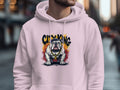 In focus against a softly blurred urban street scene, someone is wearing a light pink Garment Graphics hoodie with a bulldog design and gold chain.