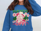 A woman sports a blue, loose-fit sweatshirt from Garment Graphics featuring a unique design: a woman in a hat, pink flowers, green HANDS, and red Wild Side OFF! text with red hearts. Ideal for standout style from the Hands off Wild Side Sweatshirts collection.