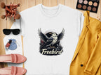 Garment Graphics white sweatshirt showcases an eagle design with Freebird emblazoned on it. Paired items include a yellow blazer, pink loafers, a sunglasses pouch with cosmetics and makeup brushes, and an eyeshadow palette—all elegantly arranged on a wooden surface.