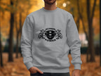 A person in a light gray Scania Power sweatshirt from Garment Graphics, featuring two stylized lion heads, stands in an outdoor park with blurred autumn leaves and trees.