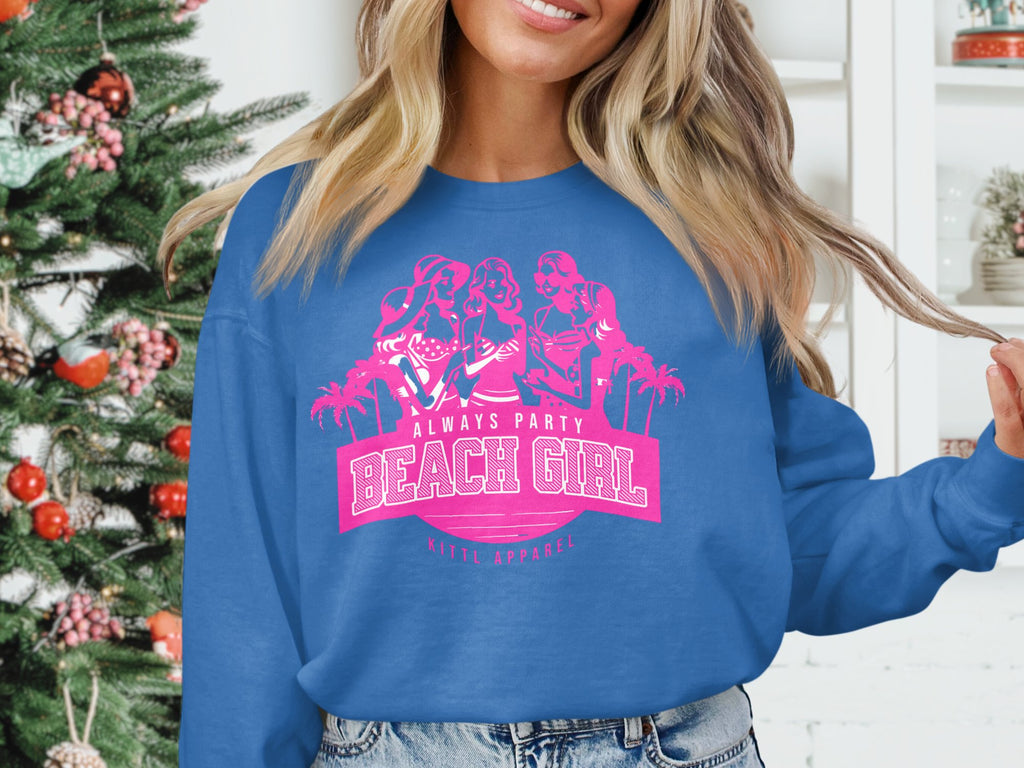 A person wears a blue sweatshirt with pink text, Always Party Beach Girl, Garment Graphics, featuring images of three girls and palm trees. A decorated Christmas tree adds a festive touch to the scene.