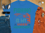 The Garment Graphics blue fishing T-shirt boldly states Fishing Is My Anger Management in vibrant green and orange, featuring a fish and lure. Paired with jeans, sunglasses, headphones, a watch, and a brown shirt on wood—ideal for any fishing enthusiasts casual day out.
