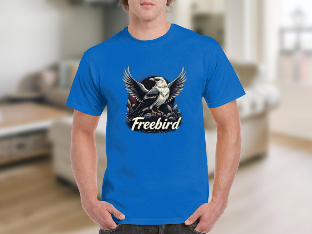 Wearing a bold, 100% cotton Garment Graphics T-shirt featuring a bird with spread wings on branches, and Freebird printed below, one evokes freedom in an out-of-focus indoor setting.