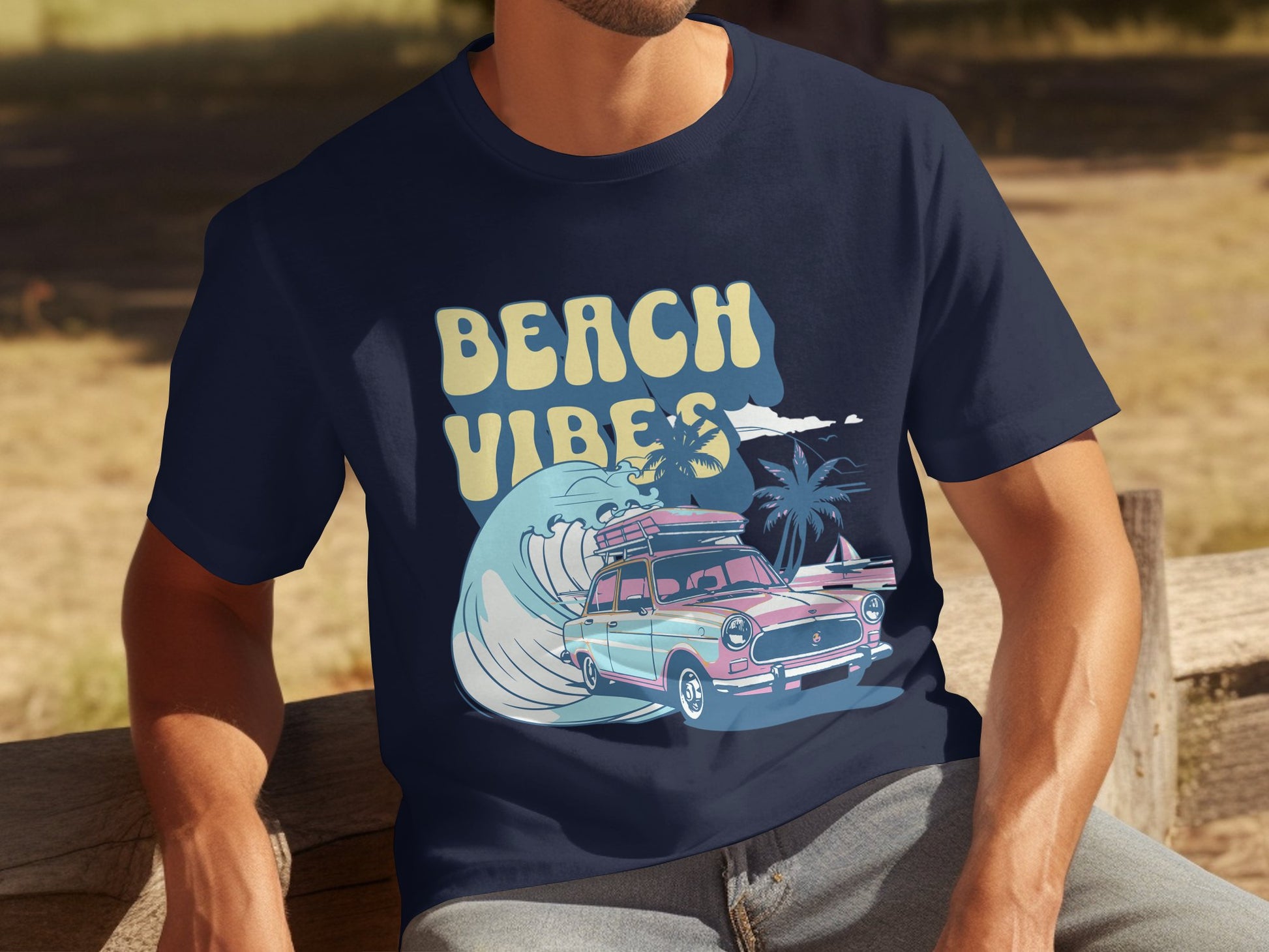 A person relaxes on a wooden bench wearing Garment Graphics navy blue graphic t-shirt adorned with BEACH VIBES in yellow, showcasing a classic car, surfboard, large wave, and palm trees—capturing a retro beach theme.