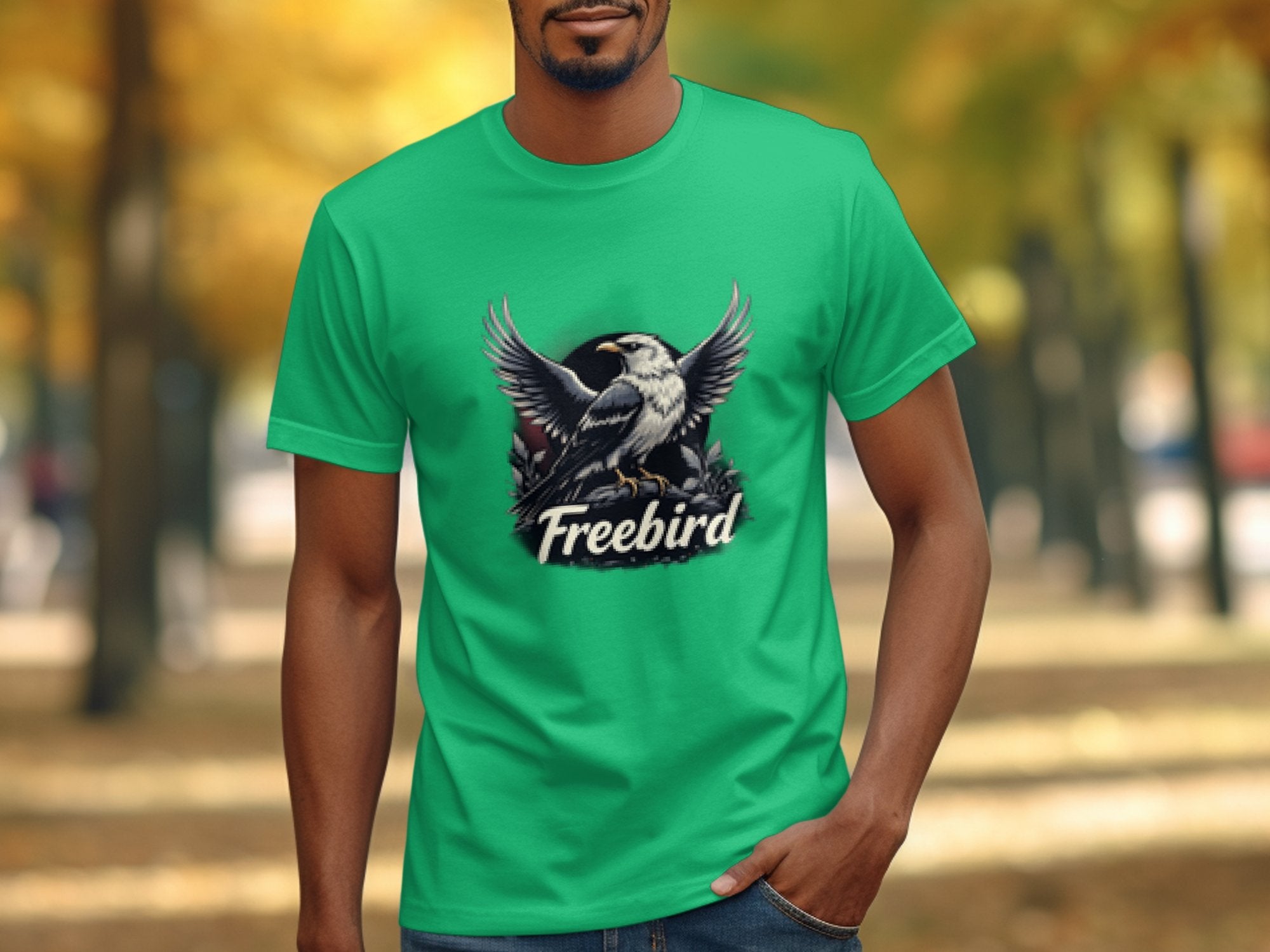Wearing a striking green T-shirt by Garment Graphics, featuring 100% cotton fabric and a bold bird illustration with Freebird, a person stands on a tree-lined path amidst vibrant autumn colors.