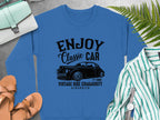 Garment Graphics offers a blue sweatshirt with a black graphic of a classic car and the text Enjoy Vintage Ride, Aircooled, Estd 1980. Its stylishly combined with a purse, sandals, wristwatch, and striped shirt on a gray surface.