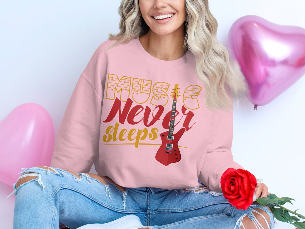 A person with long blonde hair sits cross-legged, smiling while holding a red rose. They wear Garment Graphics trendy pink sweatshirt with a guitar design and Music Never Sleeps. Pink heart-shaped balloons float in the background, ideal for music enthusiasts.