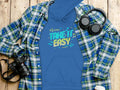 Garment Graphics captures casual style with a blue hoodie featuring Take It Easy in vibrant font over a plaid shirt on wood. A camera, headphones, and a white cup accompany the look, while musical notes and arrows add flair to this comfortable fashion statement.