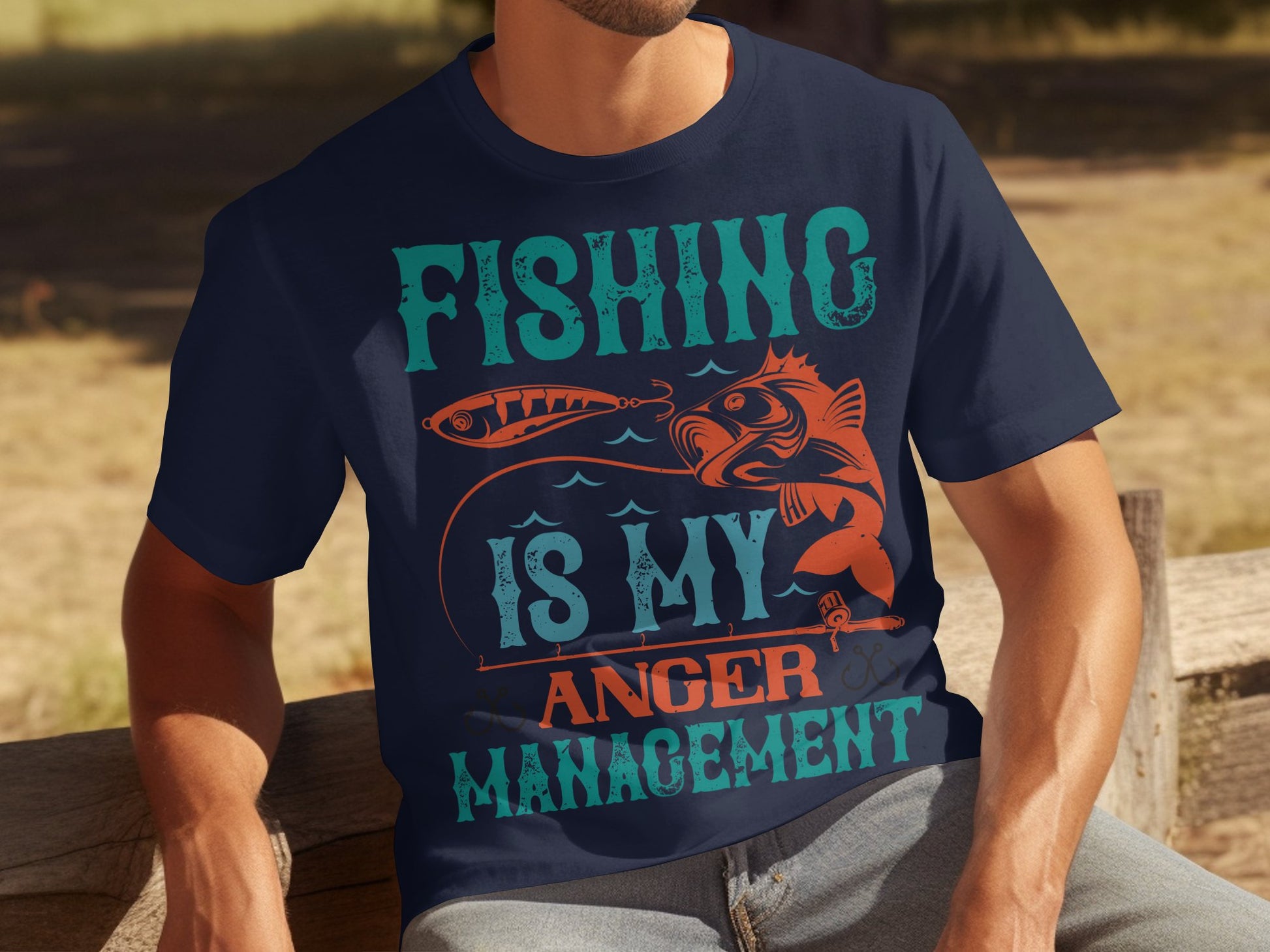 A fishing enthusiast sits on a wooden bench in a navy blue Garment Graphics T-shirt featuring orange and teal text and images of a fish and lure, declaring, Fishing Is My Anger Management.