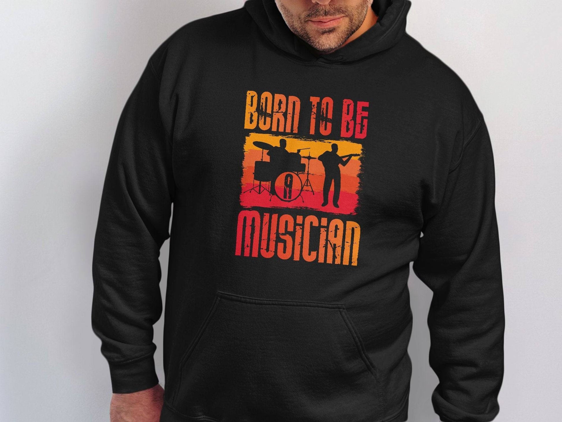 A person is stylishly clad in a black hoodie from Garment Graphics Unisex Fashion Hoodies, featuring silhouetted drummer and guitarist designs. Born to be a Musician is boldly displayed in multicolored letters on a white background—ideal for every music enthusiast.