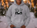 Sporting Garment Graphics gray hoodie featuring a race car and checkered flags, the wearer embraces a racing theme against softly blurred lights and falling snowflakes, evoking a cozy winter feeling.