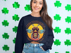 A woman smiles in a dark Bee Yourself Summer Edition sweatshirt from Garment Graphics, standing against a wall with green shamrocks. The unisex sizing means everyone can enjoy this cozy reminder to always be true to oneself.