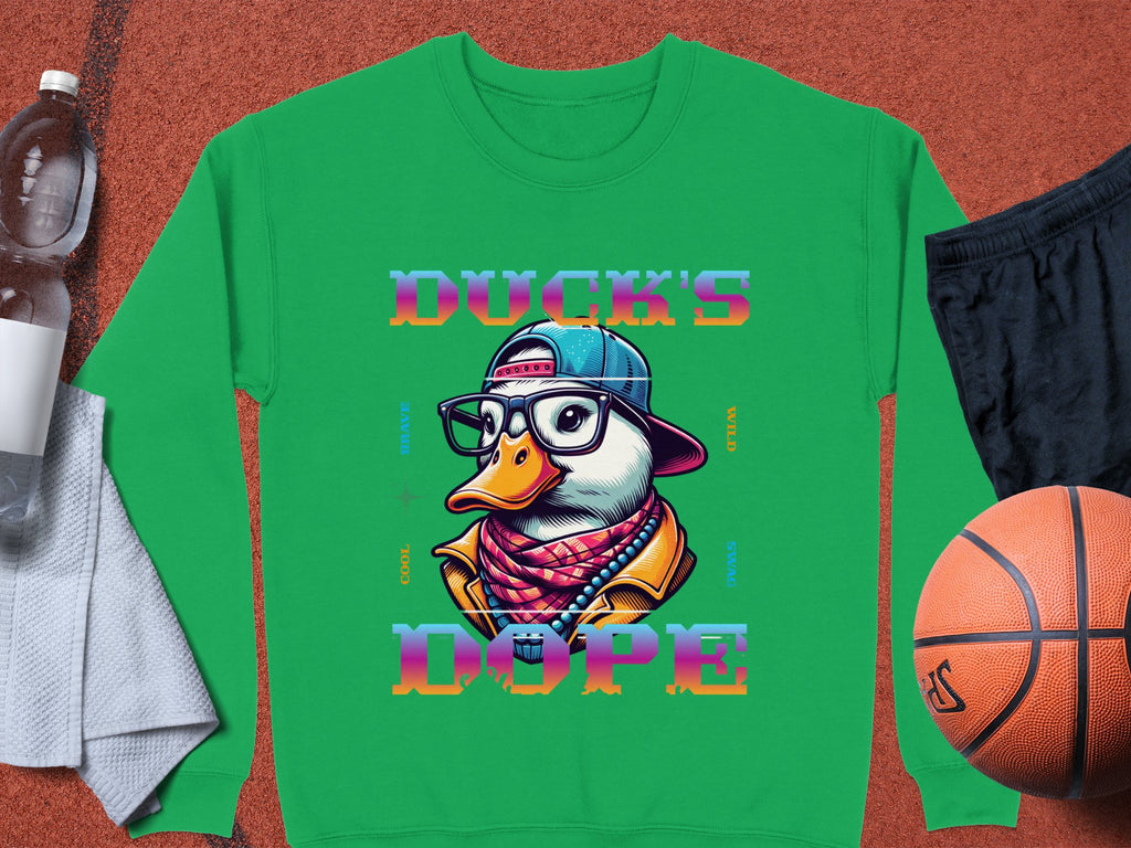 The Garment Graphics green sweatshirt from the Brave Cool Swag collection features a cartoon duck with glasses, a hat, and scarf, alongside DUCKS DOPE in vibrant text. Made of medium-heavy fabric with unisex sizing, it pairs well with a water bottle, towel, basketball, and black shorts.