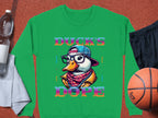 The Garment Graphics green sweatshirt from the Brave Cool Swag collection features a cartoon duck with glasses, a hat, and scarf, alongside DUCKS DOPE in vibrant text. Made of medium-heavy fabric with unisex sizing, it pairs well with a water bottle, towel, basketball, and black shorts.