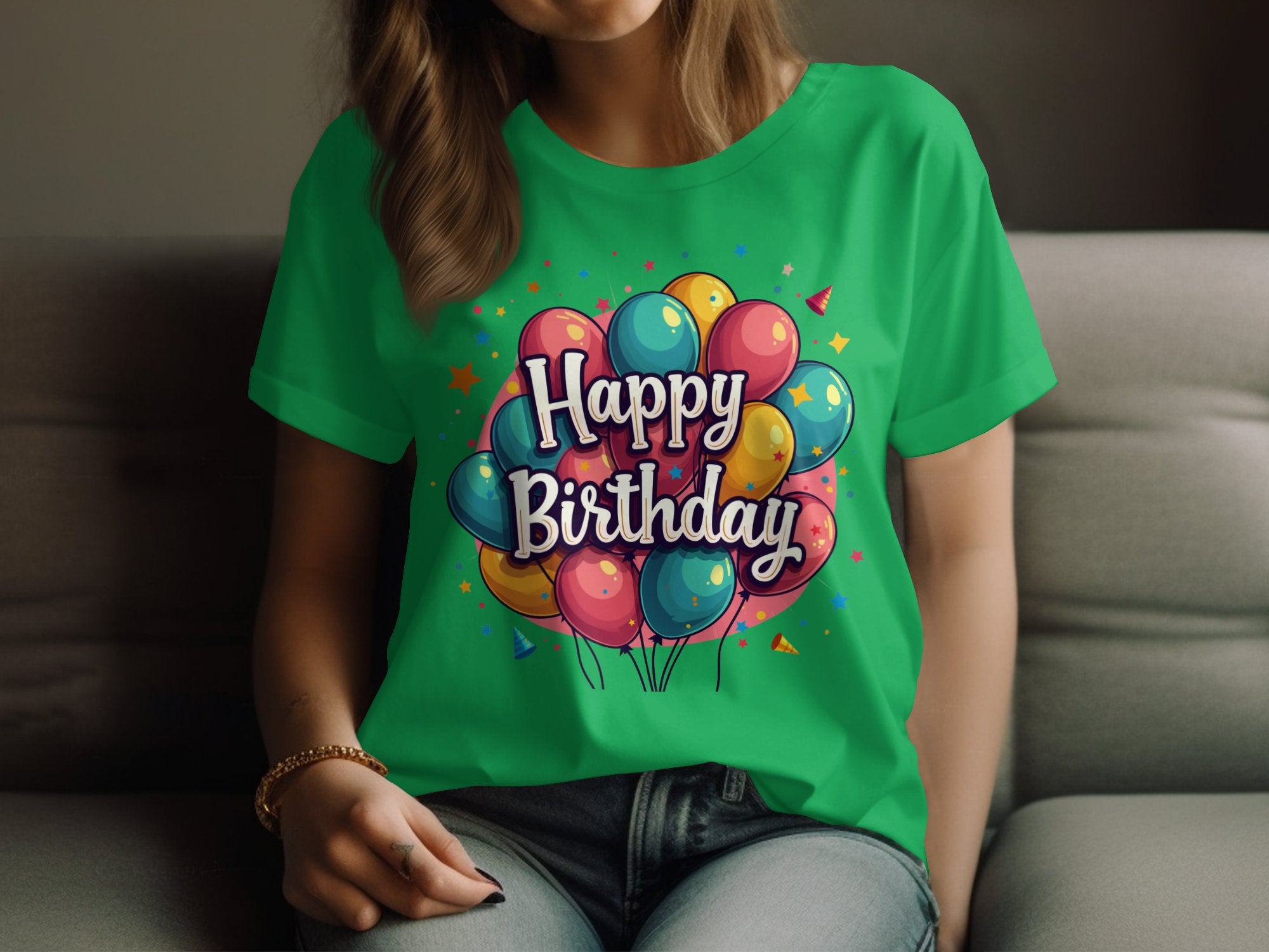 A woman sits on a sofa in a vibrant Garment Graphics 100% cotton green t-shirt featuring colorful balloons and the text Happy Birthday. Casually dressed with her hair down, she rests her hands on her lap, embracing the joyful birthday ambiance.
