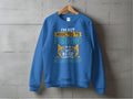 A blue unisex sweatshirt by Garment Graphics hangs on a concrete wall, showcasing the text: Im not addicted to fishing. We are just in a very committed relationship, complete with fishing-themed graphics.