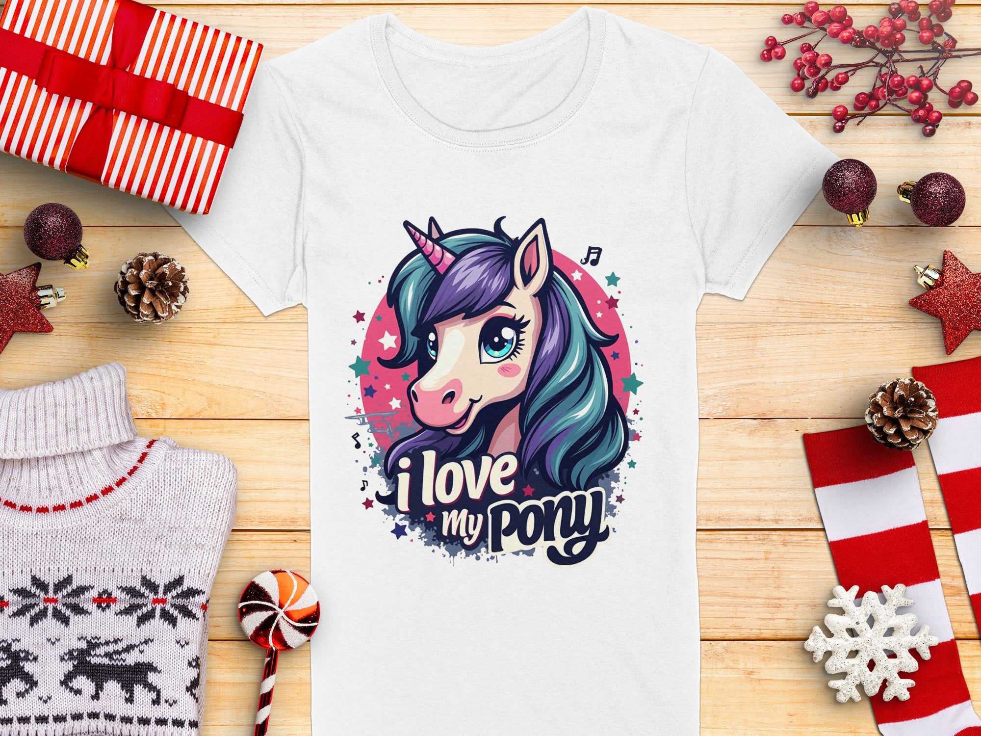 Garment Graphics offers a white T-shirt featuring a vibrant unicorn graphic with I Love My Pony, accompanied by stars and musical notes. Its styled with wrapped gifts, pinecones, ornaments, a Christmas sweater, and candy cane on wood—ideal for unicorn enthusiasts.