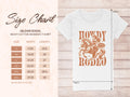 The Garment Graphics Howdy Rodeo T-shirt, featuring a woman on horseback, is available in sizes S to 3XL with a detailed size chart for womens width and length in inches, all presented on a clean white background.