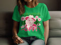 A person is seated wearing a green Garment Graphics T-shirt with a bold design featuring an illustrated cowboy in a hat, surrounded by flowers, Hands Off! and Wild Side phrases, and accented with hearts and floral elements to enhance its unique style.