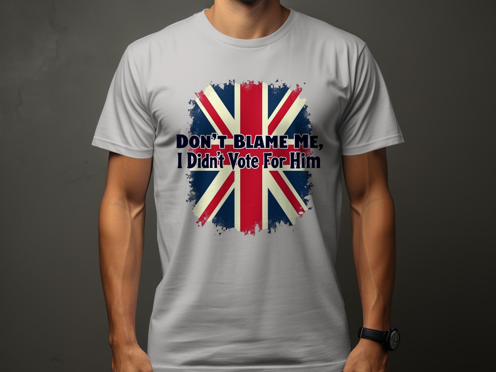 A person in a classic fit Garment Graphics T-shirt displays a Union Jack design with the prominent statement, DONT BLAME ME, I Didnt Vote For Him, vividly printed on a plain, dark background.