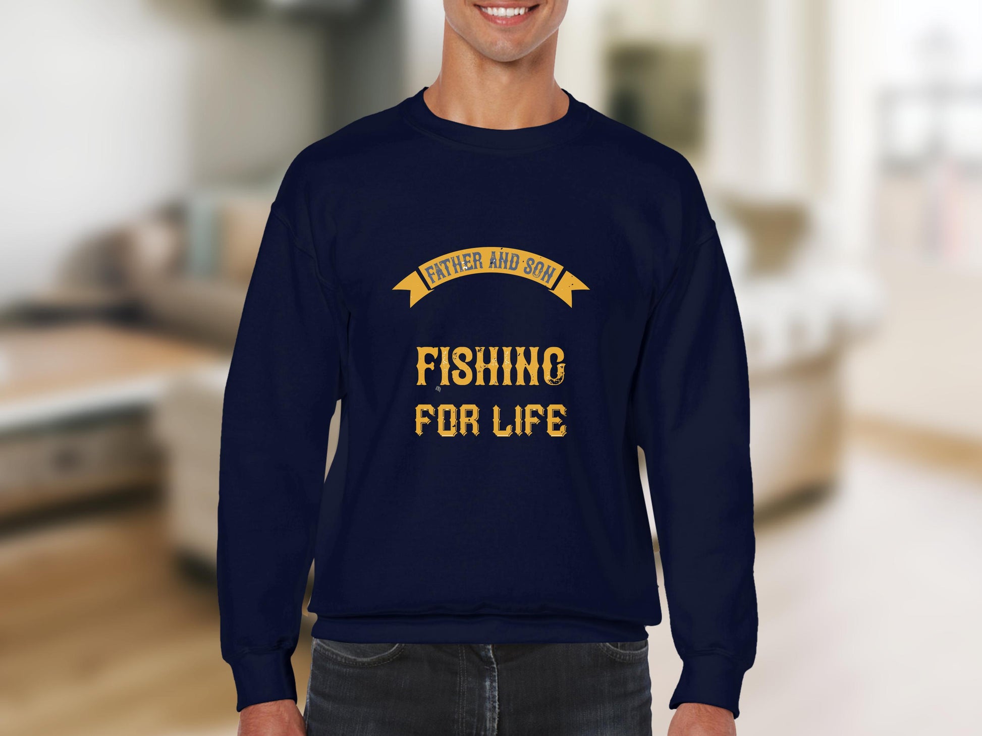 A person wears a Garment Graphics navy blue sweatshirt, featuring bold yellow Father and Son Fishing for Life text against an indoor setting with a sofa and light-colored walls.