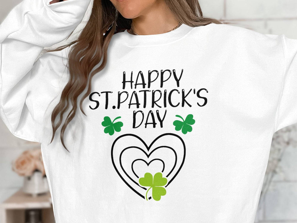 A person wears a Garment Graphics sweatshirt with Happy St. Patricks Day in black, featuring a vibrant clover design with green shamrocks and heart shapes, set against festive surroundings. Their head is partially out of frame, highlighting their long brown hair.