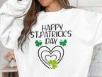 A person wears a Garment Graphics sweatshirt with Happy St. Patricks Day in black, featuring a vibrant clover design with green shamrocks and heart shapes, set against festive surroundings. Their head is partially out of frame, highlighting their long brown hair.