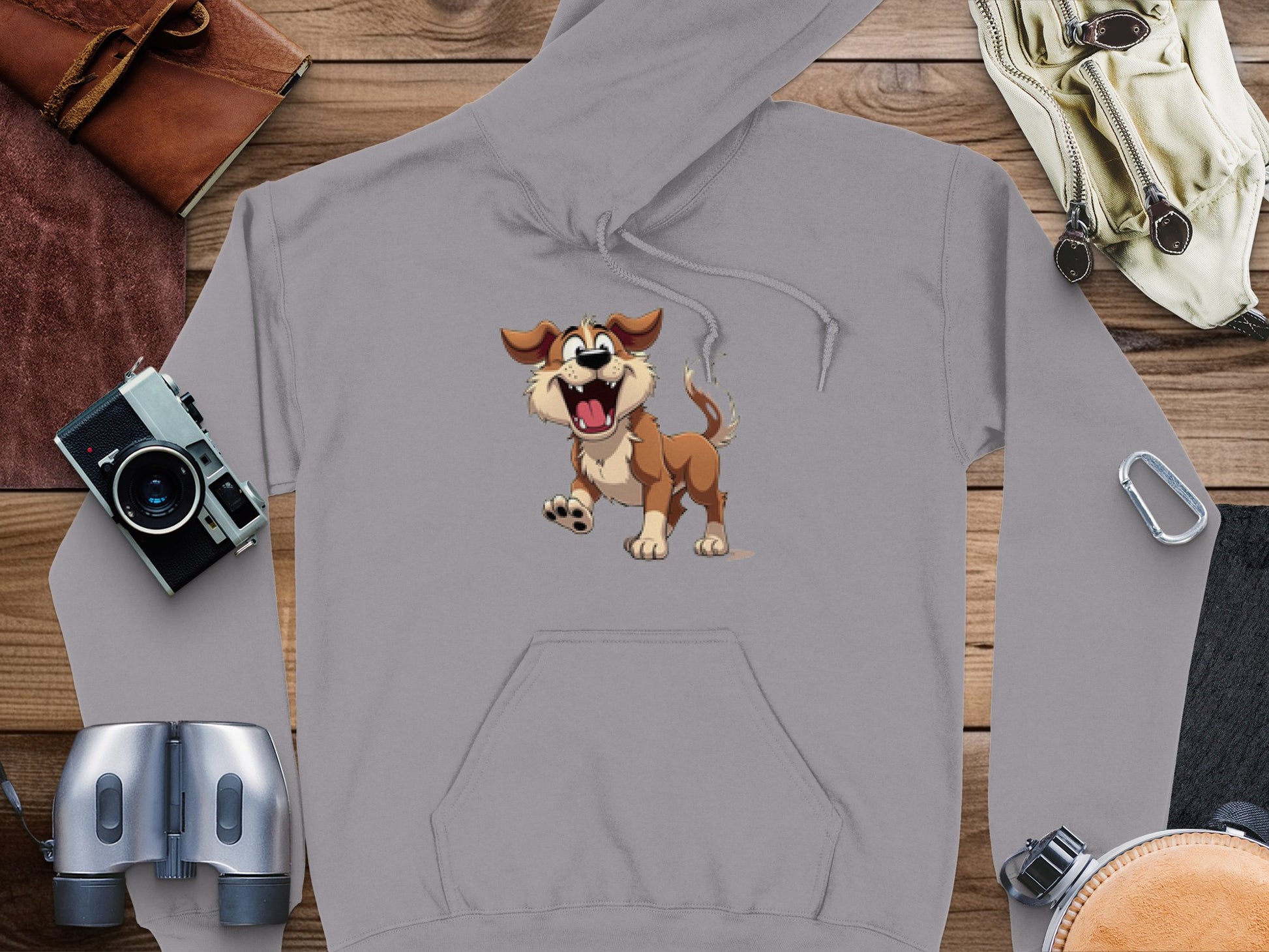 The Garment Graphics gray hoodie boasts a central cartoon dog graphic, ideal for dog lovers. Its fun design is enhanced by a vintage camera, binoculars, leather-bound books, and gloves on wooden accents, adding charm to any casual outfit.