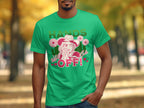 A man wears Garment Graphics bold green t-shirt featuring a graphic of a hatted person with flowers, striking HANDS OFF! text, and smaller wild and safe letters. This classic fit shirt stands out against the parks trees and blurred paths.