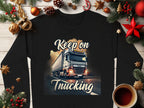 Garment Graphics unisex sweatshirt features a black base with a truck illustration under bright skies, the phrase Keep on Trucking, festive decorations like pine branches, ornaments, and a coffee cup.