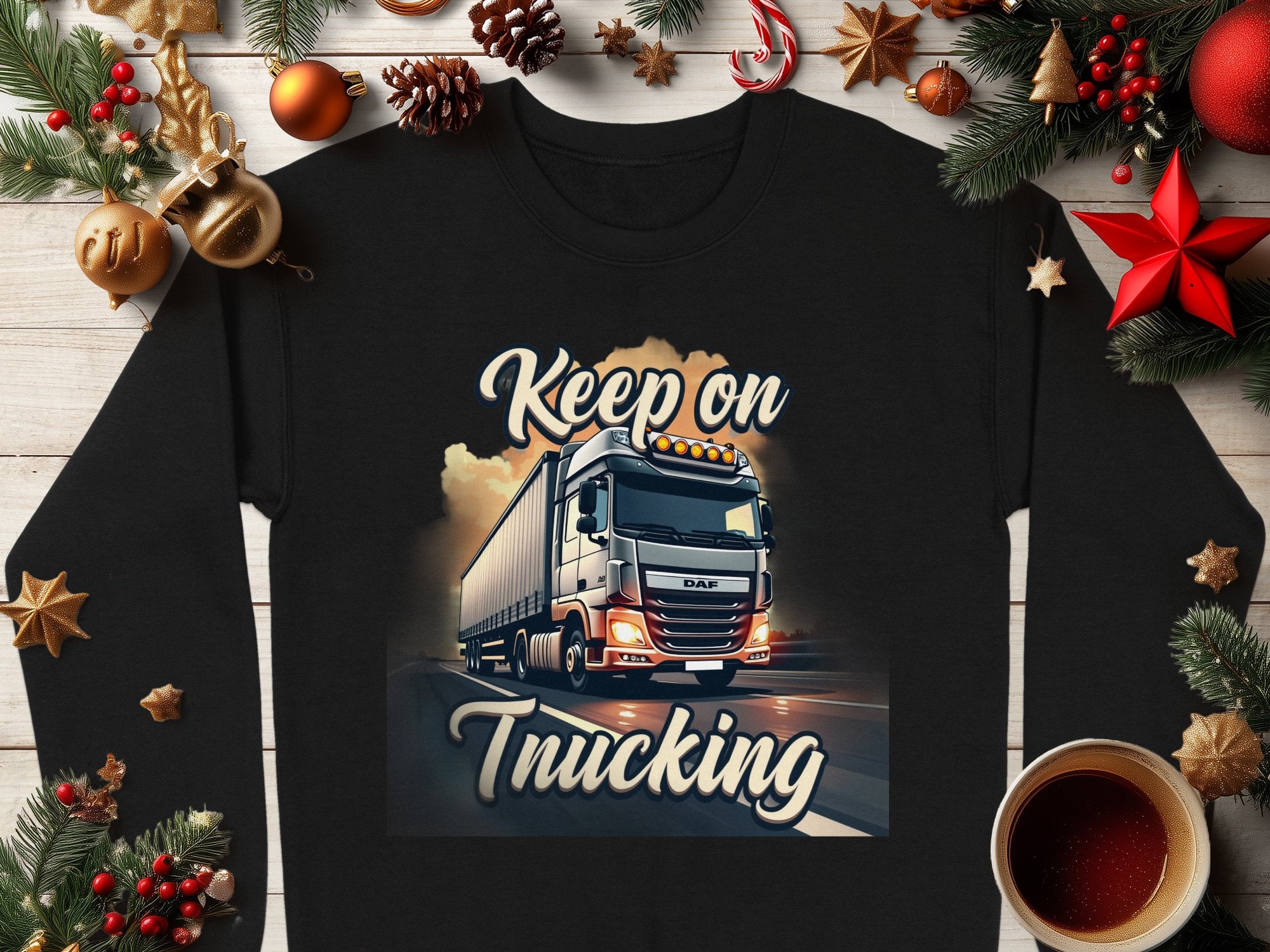 Garment Graphics unisex sweatshirt features a black base with a truck illustration under bright skies, the phrase Keep on Trucking, festive decorations like pine branches, ornaments, and a coffee cup.