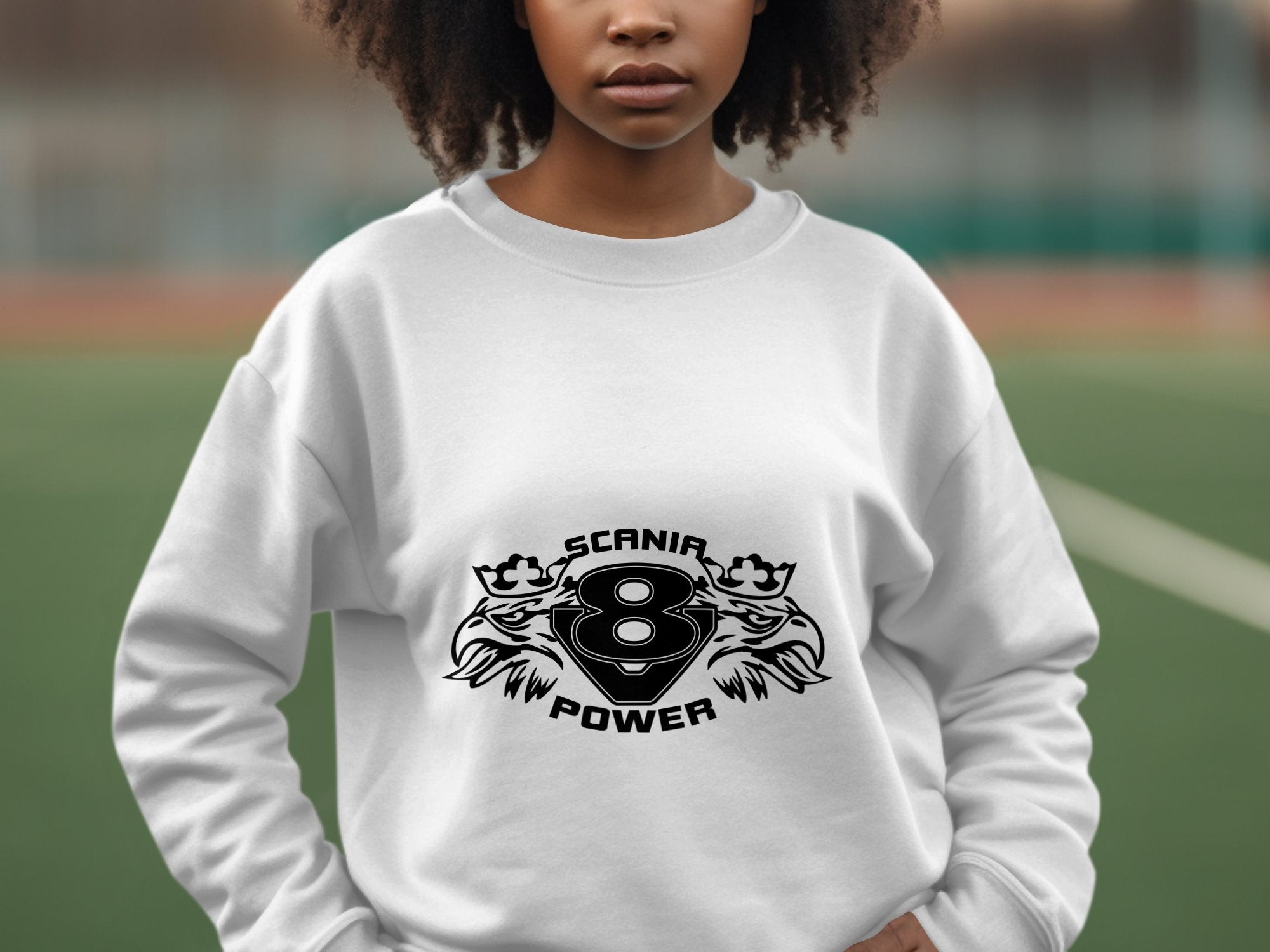 A person outdoors dons a stylish white sweatshirt from Garment Graphics with SCANIA POWER, two stylized animals, and the number eight printed on it. The blurred sports field background enhances the allure of this Scania Power V8 sweatshirt.