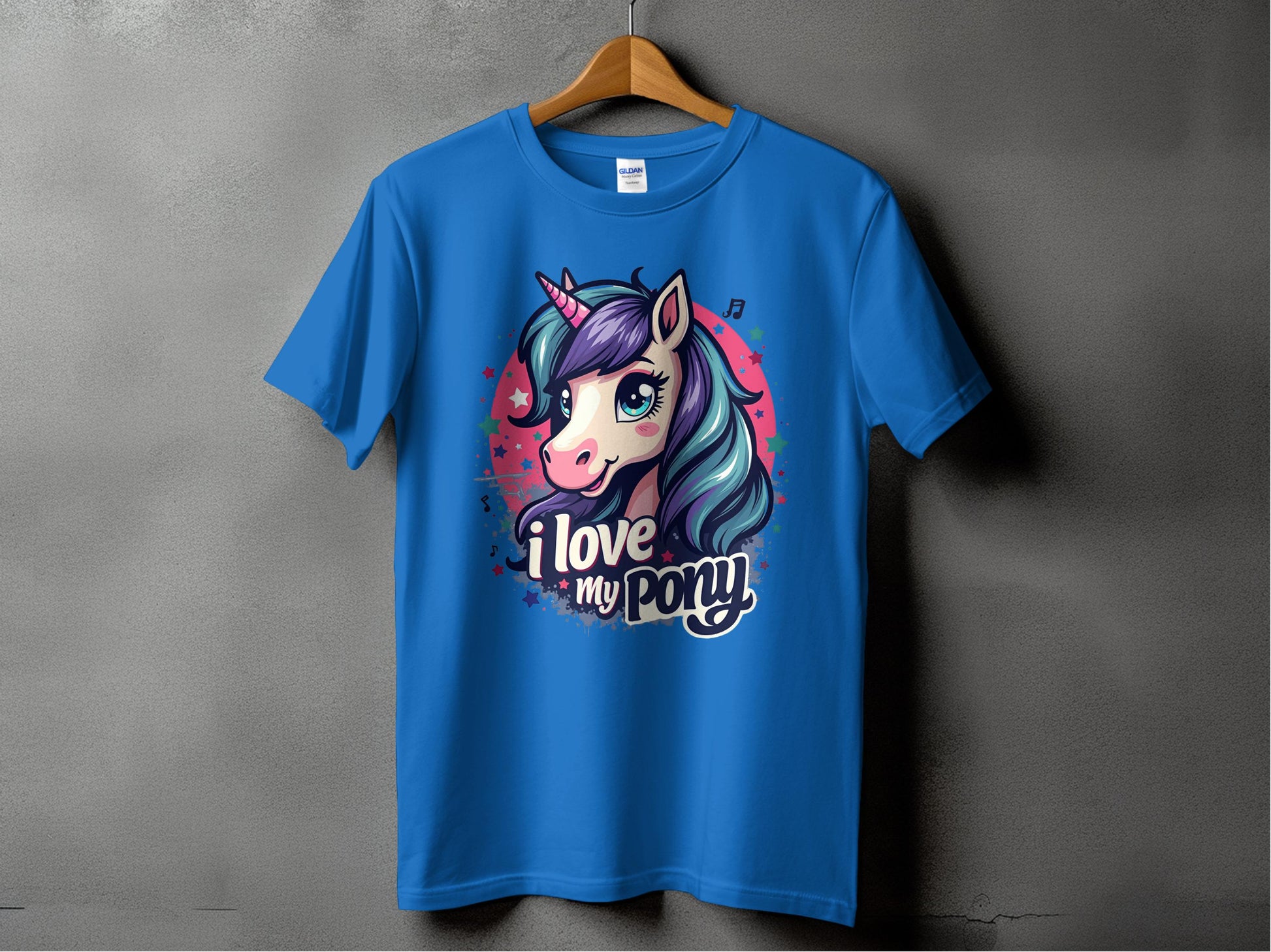A blue Garment Graphics T-shirt is displayed on a wooden hanger with a gray backdrop. It features a vibrant unicorn head with purple hair and a horn, surrounded by stars, and reads I love my pony at the bottom—ideal for unicorn enthusiasts!.