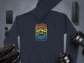 A Garment Graphics navy retro hoodie with a Woodstock 1969 graphic print is laid out on a gray surface. Nearby are essentials like a smartphone, smartwatch, shoes, wireless speaker, and dumbbells, blending technology and fitness styles.