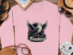 The Garment Graphics Freebird Graphic Sweatshirt showcases a vibrant pink design with an eagle above Freebird. Paired with travel essentials like a camera and sunglasses, this unisex sweatshirt embodies the spirit of adventure.
