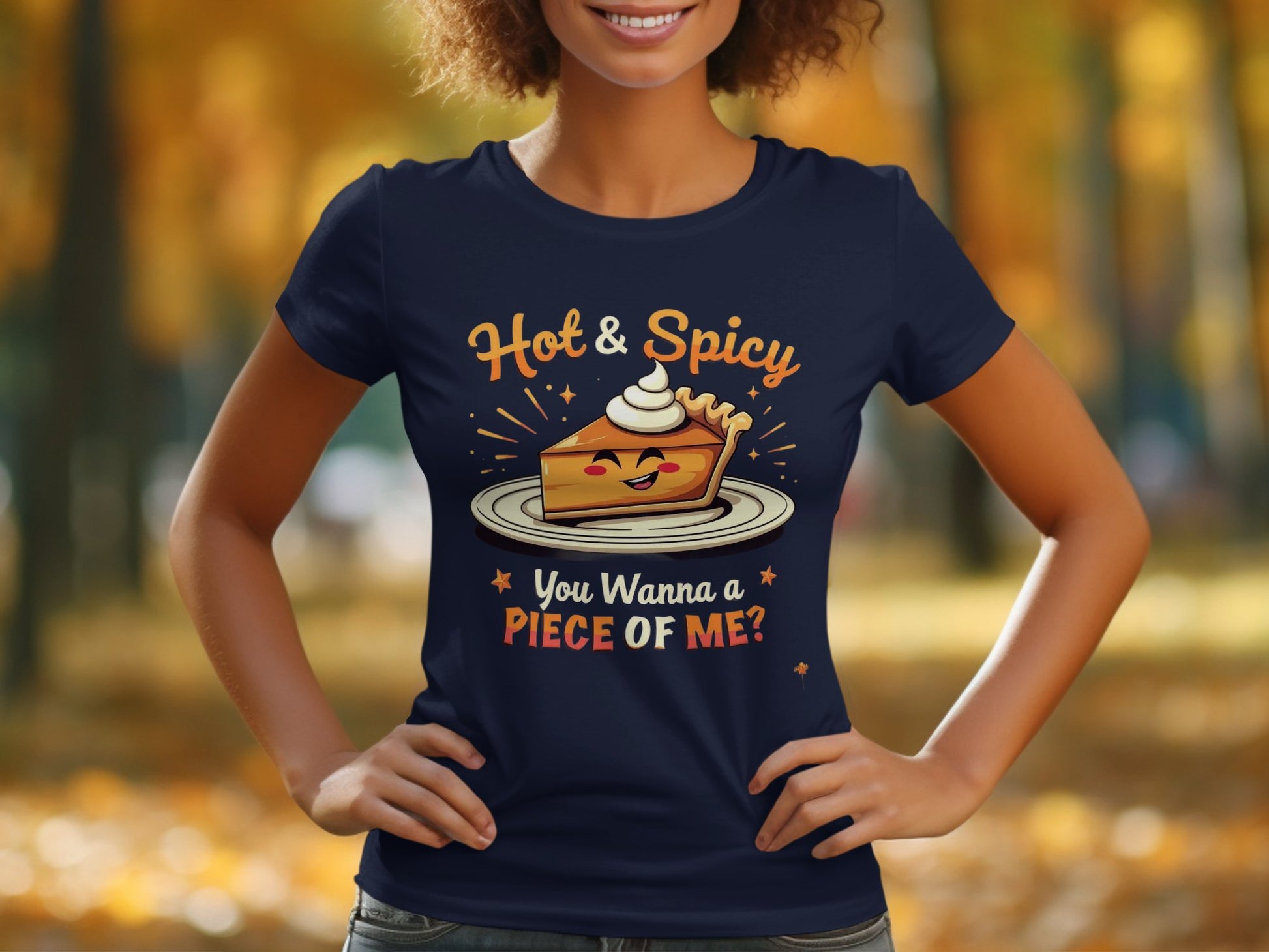 In a lively park with blurred autumn foliage, a person wears a navy T-shirt featuring Garment Graphics cheeky design: a smiling pie with whipped cream and the text Hot & Spicy You Wanna Piece of Me? This womens T-shirt is ideal for casual outings, combining comfort and flair.