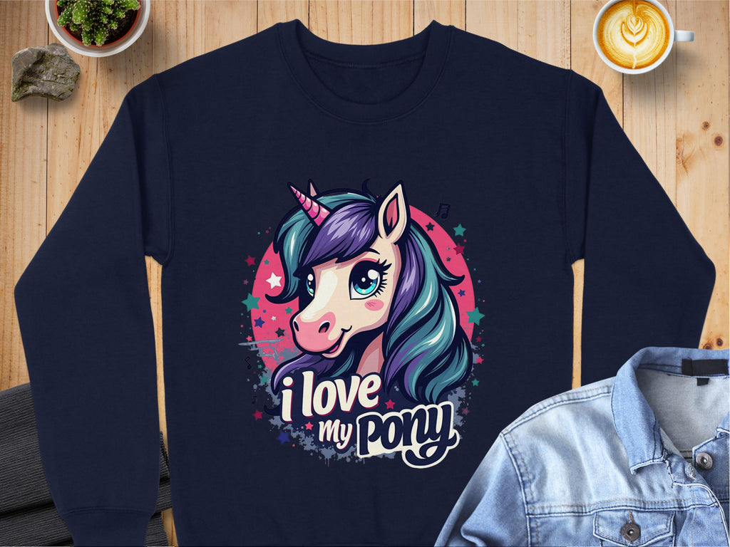 A Garment Graphics navy blue sweatshirt with a colorful unicorn design featuring a purple mane, teal details, and star accents. The text I love my pony is beneath the unicorn. Displayed on a wooden surface.