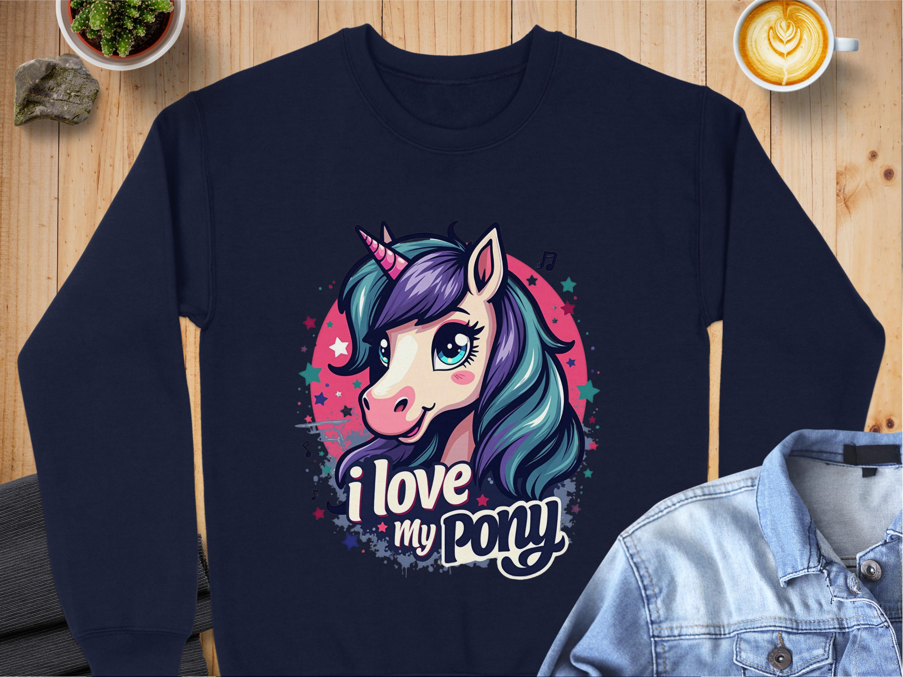 A Garment Graphics navy blue sweatshirt with a colorful unicorn design featuring a purple mane, teal details, and star accents. The text I love my pony is beneath the unicorn. Displayed on a wooden surface.