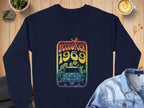 Garment Graphics navy blue sweatshirt has a retro vibe with a vintage-style van, flowers, and bird design. Woodstock 1969 is in rainbow colors. Photographed beside a latte and denim jacket, it captures the legendary Woodstock festivals essence.