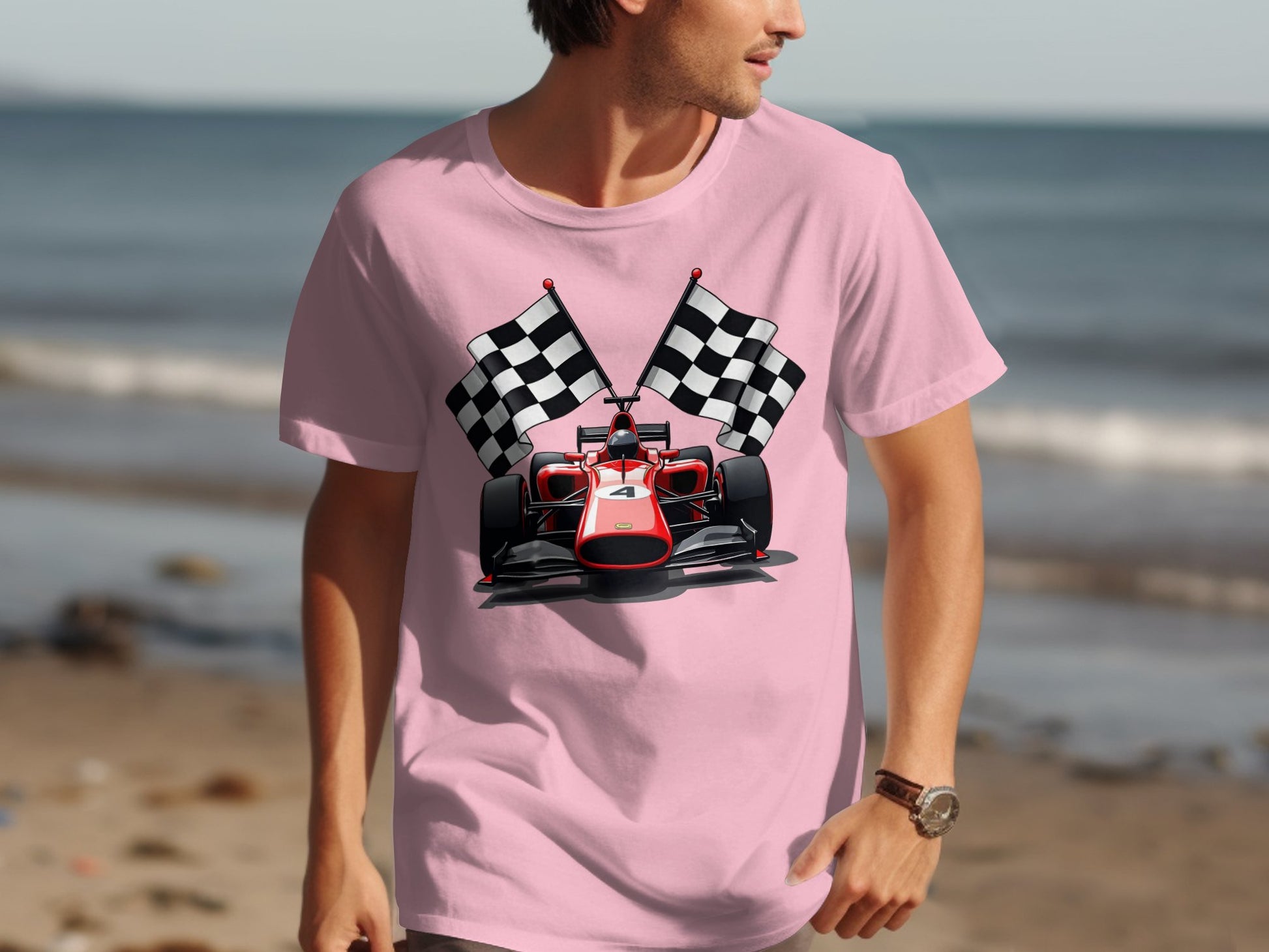 Wearing Garment Graphics light pink T-shirt, featuring a red racing car and two checkered flags, an individual stands at the seaside with sand and ocean creating a perfect motorsport backdrop.